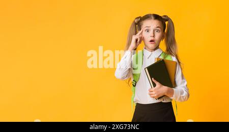 Peinlich Elementary Student auf Kamera Holding Bücher auf gelbem Hintergrund Stockfoto