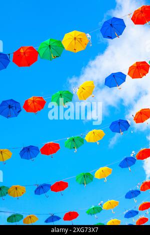 Bunte Regenschirme hängen am Himmel. Regenschirme in verschiedenen Farben und Größen schaffen eine lebendige und lebhafte Atmosphäre Stockfoto