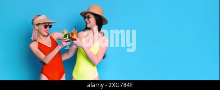 Zwei Frauen in Badeanzügen, die mit Cocktails vor blauem Hintergrund toasten Stockfoto