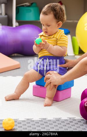 Ein kleines Kind mit Körperhypotonie nimmt mit Unterstützung eines Therapeuten an einer Physiotherapie Teil, die sich auf motorische Fähigkeiten konzentriert Stockfoto