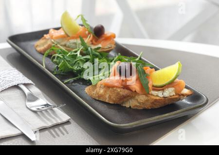 Bruschetta mit Lachs. Vollkornbrot mit Lachs, Käse und einer Scheibe Zitrone auf hellem Hintergrund in einem Restaurant. Gesundes Lebensmittelkonzept. Stockfoto