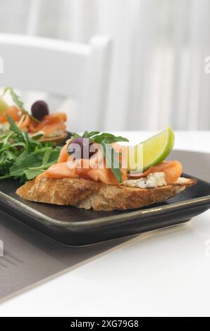 Bruschetta mit Lachs. Vollkornbrot mit Lachs, Käse und einer Scheibe Zitrone auf hellem Hintergrund in einem Restaurant. Gesundes Lebensmittelkonzept. Stockfoto