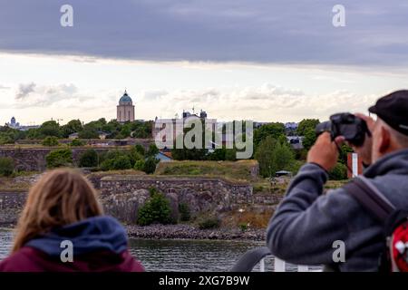Kreuzfahrtpassagiere sehen und fotografieren die Meeresfestung Suomenlinna in Helsinki, Finnland, von einem offenen Deck an Bord. Stockfoto