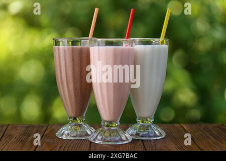 Set mit verschiedenen köstlichen Milchshakes in Gläsern mit Stroh auf dem Tisch draußen Stockfoto