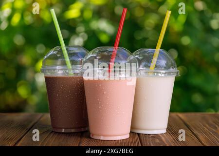 Set aus verschiedenen leckeren Milchshakes in Einweg-Plastikgläsern mit Stroh auf dem Tisch draußen Stockfoto