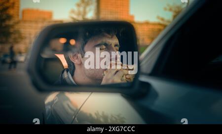 Auto-Seitenspiegel Blick Kaukasischer Mann Guy Taxifahrer essen Burger im Auto männlich hungrig essen Junk Fast Food Mittagspause Genießen Sie Geschmack köstlich Stockfoto