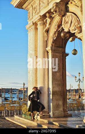 Eine glamouröse, gut gekleidete Frau sitzt in einem leeren Café im Freien und genießt am frühen Morgen die Aussicht auf Venedig Stockfoto