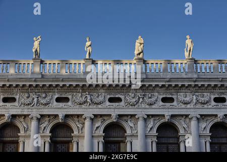 Biblioteca Nazionale Marciana, Details der Fassade, kunstvoller Fries und Statuen heidnischer Gottheiten auf der Balustrade vor blauem Himmel Stockfoto