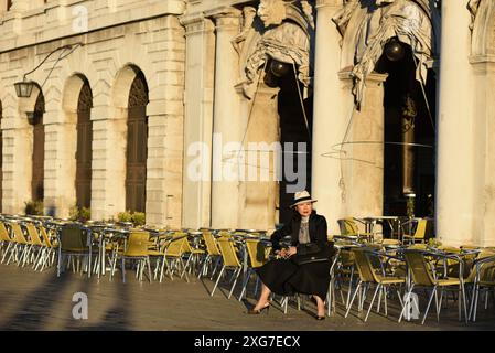 Eine glamouröse, gut gekleidete Frau sitzt in einem leeren Café im Freien und genießt am frühen Morgen die Aussicht auf Venedig Stockfoto