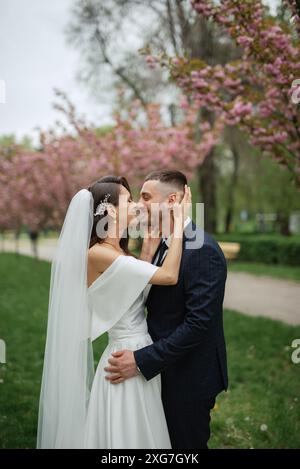 Frisch Vermählte wandern im Park auf dem Gras inmitten von Kirschblüten Stockfoto