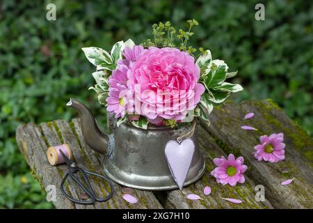 Blumenarrangement mit rosa Rose Prinzessin Alexandra von Kent, Chrysanthemen und Spindelbusblättern in Vintage-Teekanne Stockfoto