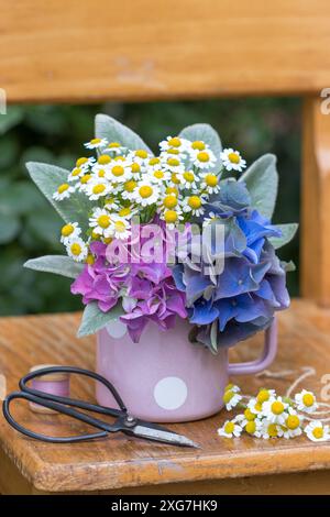 Strauß von Hortensie- und Fieberblüten in einem Emailbecher Stockfoto