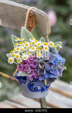 Blumenstrauß mit Hortensie, Fieber und Lammohrblättern in einem Topf, der auf dem Gartenstuhl hängt Stockfoto