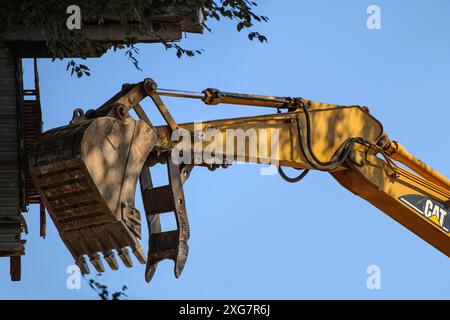 Der hydraulische Arm eines Baggers erleichtert die Arbeit eines Holzhauses, während er Land zur Vorbereitung auf eine neue Entwicklung räumt. Stockfoto