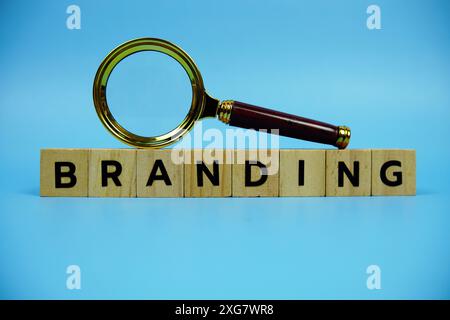 Branding mit Holzblöcken Buchstaben und Vergrößerungsglas auf blauem Hintergrund Stockfoto