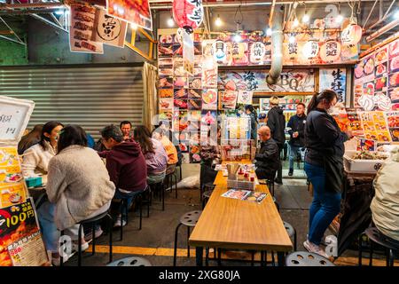 Abends sitzen Gäste an Tischen auf dem Bürgersteig vor einem japanischen Restaurant Izakaya im beliebten Nachtleben-Viertel Ueno Ameyoko, Tokio. Stockfoto