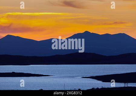 Atemberaubender Sonnenuntergang über dem ruhigen Wasser und den zerklüfteten Hügeln der Insel Antiparos, Griechenland, der ein warmes Licht über die Landschaft wirft. Stockfoto