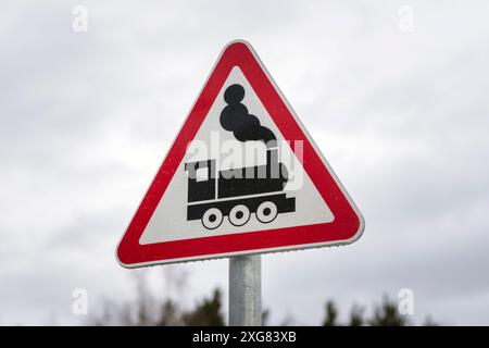 Nahaufnahme eines dreieckigen Zugkreuzschildes mit einer alten Lokomotivabbildung an einem bewölkten Tag. Stockfoto
