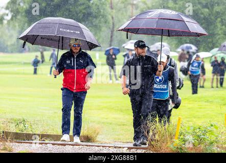 07 Juli 2024, Bayern, München/Eichenried: Golf: BMW International Open, Runde 4, Schottland Ewen Ferguson (l) und England Jordan Smith gehen Seite an Seite mit Regenschirmen. Foto: Ulrich Gamel/kolbert-Press/dpa Stockfoto