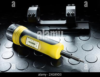 Drehmomentwerkzeug, das in Pfund misst, neben einem großen Sockel für die Befestigung eines Gewehrfernrohrs an einer Schusswaffe. Stockfoto
