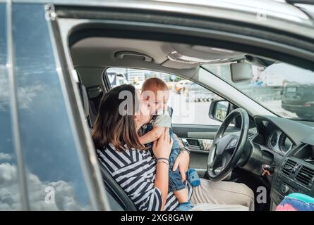 Mutter und Baby sitzen im geparkten Auto, während das Baby spielerisch das Lenkrad hält. Die Szene fängt den zärtlichen Familienmoment ein, betont Bindung, Erkundung, A Stockfoto