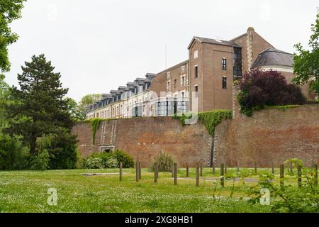 Cambrai, Frankreich - 21. Mai 2023: Ein historisches Gebäude in Cambrai, Frankreich, ist von einer hohen Backsteinmauer umgeben, die mit Grün geschmückt ist und einen Blick auf i freigibt Stockfoto