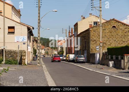 Langeac, Frankreich - 28. Mai 2023: Eine ruhige Straße in Langeac, Frankreich, an einem sonnigen Tag. Ein rotes Auto fährt entlang der Straße, vorbei an einer Reihe traditioneller Straßen Stockfoto