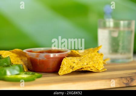 Nachos mit roter, heißer Paprika-Sauce auf einem Holzständer, geschnittene ​​green-Paprika und ein Getränk vor dem Fernseher mit einem Fußballspiel Stockfoto