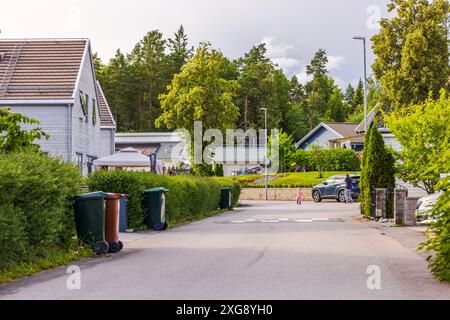 Wohngegend mit Häusern, Bäumen, Mülltonnen, geparktem Auto und Menschen, die am Sommertag in der Vorstadt spazieren gehen. Schweden. Stockfoto