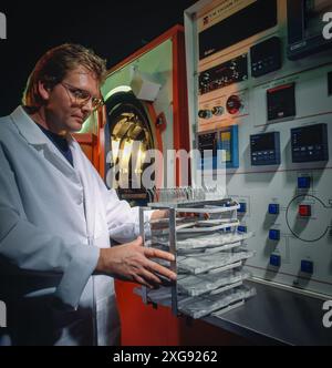 Wissenschaftler in Laborbeschichtung, die industrielle Gefriertrocknungsmaschine betreibt und Probenschalen in die Vakuumkammer mit digitalem Bedienfeld einsetzt Stockfoto
