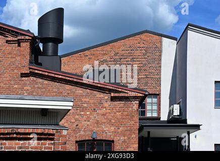 Das Bild zeigt ein modernes Gebäude mit einer Mischung aus roten Ziegelsteinen und weißen Betonwänden mit einer markanten schwarzen Lüftungsrohrstruktur gegen eine blende Stockfoto