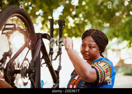 Junge Frau im Freien, die Fahrradreifen mit professioneller Ausrüstung repariert. afroamerikanerin hält das Rad im Hof zur Wartung. Stockfoto