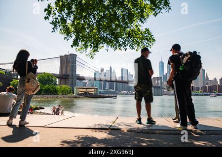 Langzeitaufnahme der Brooklyn Bridge und der Skyline von New York vom Pebble Beach über den East River an einem klaren Frühlingsmorgen. Zufallsmenschen in Stockfoto