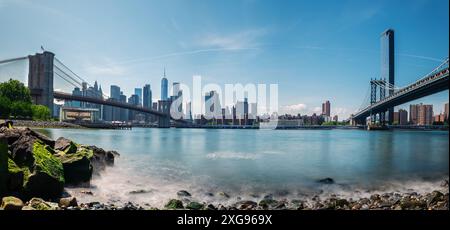 Langzeitaufnahme der Brooklyn Bridge und der Skyline von New York vom Pebble Beach über den East River an einem klaren Frühlingsmorgen. Stockfoto