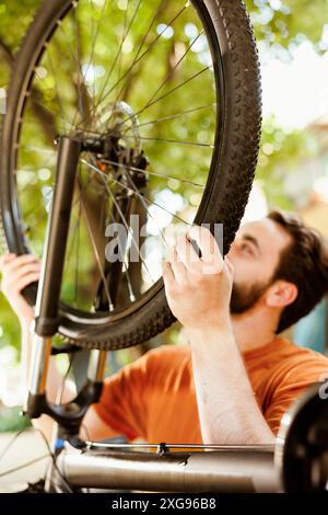 Aktiver junger Mann, der während des Sommers mit Werkzeugen auf dem Hof jährliche Wartung am Fahrrad durchführt. Gesunder sportliebender Mann, der Radrad für Sommersportfahren sichert. Stockfoto