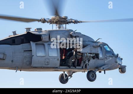 240705-N-AR554-1122 PAZIFISCHER OZEAN (5. Juli 2024) Naval Air Crewman (Hubschrauber) 3rd Class Austin Chase aus Stone Mountain, Georgia, wird in einen MH-60S Sea Hawk Hubschrauber gehoben, der an den Golden Falcons der Helicopter Sea Combat Squadron (HSC) 12 befestigt ist. während eines Hebevorganges auf dem Flugdeck an Bord des einzigen vorwärtsgerichteten Flugzeugträgers der US Navy, USS Ronald Reagan (CVN 76), am 5. Juli im Pazifik. HSC 12, ursprünglich als Helicopter Anti-Submarine Squadron (HS) 2 am 7. März 1952 gegründet, ist das älteste aktive Hubschraubergeschwader der Navy. Ronald Reagan, die Fahnen Stockfoto