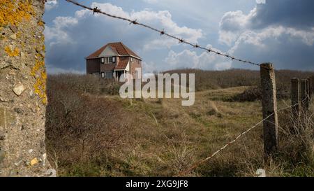 Panoramablick auf ein Haus hinter Dünen an der Nordsee mit Stacheldraht im Vordergrund Stockfoto