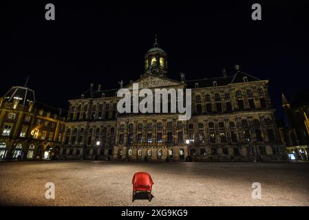 Nächtlicher Blick auf einen Roten Stuhl auf dem Damplatz mit dem Königspalast im Hintergrund - Amsterdam, Niederlande Stockfoto