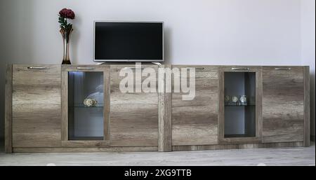 Zwei hellbraune Kommoden mit transparentem Glas, darauf befindet sich ein Fernseher, eine Vase mit einer roten Blume. Komfortable, moderne Garderobe. Das Konzept von m Stockfoto