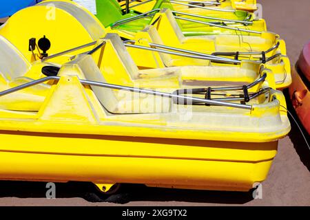 Eine Reihe von gelben Booten steht auf einem Dock. Eine Reihe hellgelber Tretboote parkte am Strand und wartete auf Fahrer Stockfoto