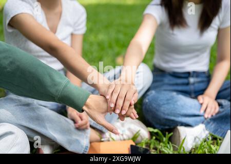 Ein Nahaufnahme-Bild einer Gruppe fröhlicher asiatischer Studenten legt die Hände zusammen, jubelt auf und zeigt Teamarbeit, während sie auf dem sitzen Stockfoto