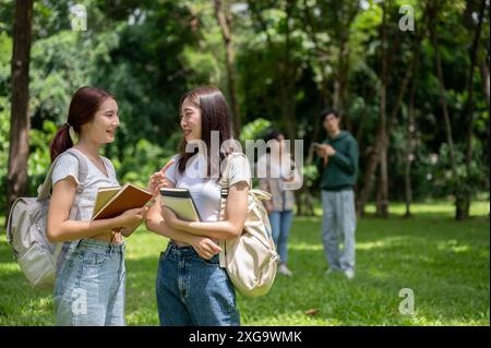 Zwei hübsche und glückliche junge asiatische Studentinnen mit Rucksäcken unterhalten sich beim gemeinsamen Spaziergang im Campus-Park. Freundschaft und Erziehung Stockfoto