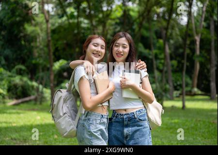 Zwei hübsche junge asiatische Freundinnen in lässiger Kleidung und Rucksäcken umarmen oder wickeln sich beim Gehen gegenseitig die Arme um die Schultern Stockfoto