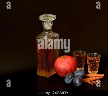 Pflaumengranatapfellikör mit Zimt und Anis auf schwarzem Hintergrund, hausgemachter Alkohol in einer Kristallschale, reife Früchte und Gewürze in der Nähe. Nahaufnahme. Stockfoto