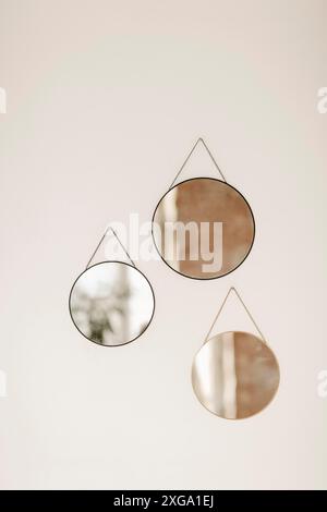 Nahaufnahme von drei runden Spiegeln in verschiedenen Größen, die an einer weißen Betonwand in der Wohnung hängen. Minimalismus in Kunst und Design, Zimmer Stockfoto