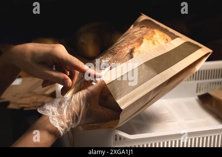 Die pflegenden Hände für Frauen packen frisches, handwerkliches Brot in eine Papiertüte mit transparentem Einsatz. Bastelbrotverpackung Stockfoto
