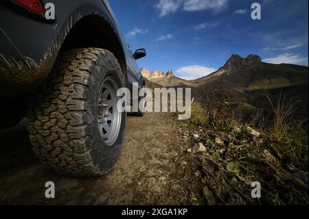 Nahaufnahme Ein großes Geländewagen-Rad steht auf einer rauen Straße in den Bergen vor dem Hintergrund von Felsen. Offroad-Touren und Offroad-Touren Stockfoto