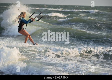 Professionelle Küchenurferin, weiße Frau, reitet bei windigem Wetter auf großen Wellen. Kitesurfen Stockfoto