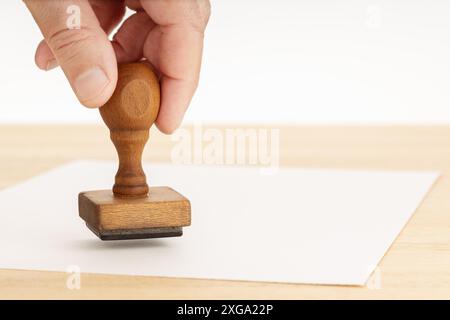 Hand mit Gummistempel und leerem Papier auf Holztisch. Weißer Hintergrund. Speicherplatz kopieren Stockfoto