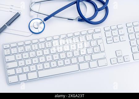 Arzttisch mit Stethoskop, Büroarbeiten und Computertastatur auf weißem Schreibtisch. Online-Gesundheitsfürsorge oder Telemedizin-Konzept. Medizinischer Hintergrund. Draufsicht Stockfoto